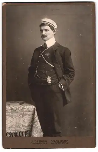 Fotografie Hugo Kühn, Baden-Baden, Student im Anzug mit Couleur und Zipfel posiert im Atelier