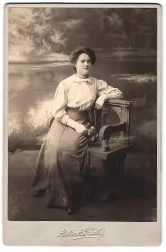 Fotografie A. Kratky, Kolin, junge Dame im Kleid sitzend auf einer Bank vor Studiokulisse