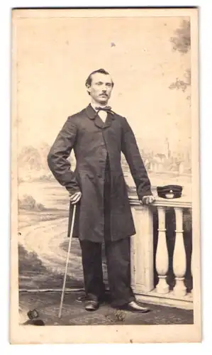 Fotografie L. Feuerrohr, Rinteln, junger Mann im Anzug mit Fliege und Flanierstock vor einer Studiokulisse