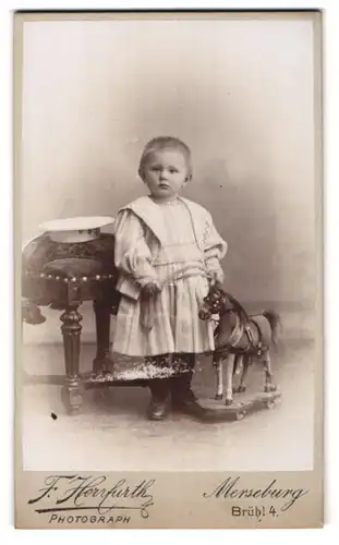 Fotografie F. Herrfurth, Merseburg, niedliches kleines Mädchen im weissen Kleid mit Spielzeugpferd