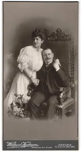 Fotografie Richard Kasbaum, Berlin, Portrait verliebtes Paar im weissen Kleid mit Halskette und im Anzug mit Moustache