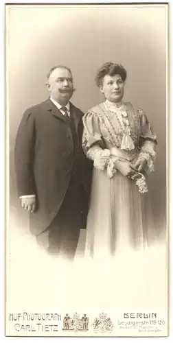 Fotografie Carl Tietz, Berlin, Leipzigerstr. 119-120, älteres Paar im Anzug und im hellen Kleid mit Brosche