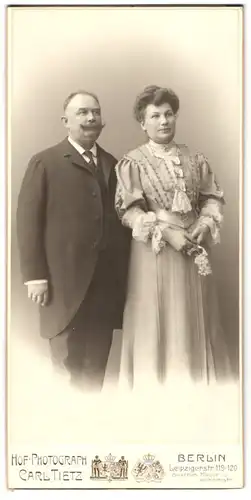 Fotografie Carl Tietz, Berlin, Leipzigerstr. 119-120, Paar im dunklen Anzug mit Moustache und im hellen Kleid mit Brosch