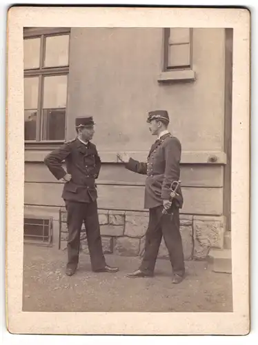 Fotografie unbekannter Fotograf und Ort, zwei österreichische Eisebahner in hitzigem Disput, Uniform mit Säbel