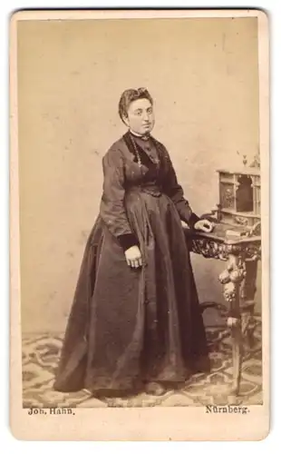 Fotografie Joh. Hahn, Nürnberg, Portrait Dame im dunklen Kleid mit Halskette steht an einem Sekretär