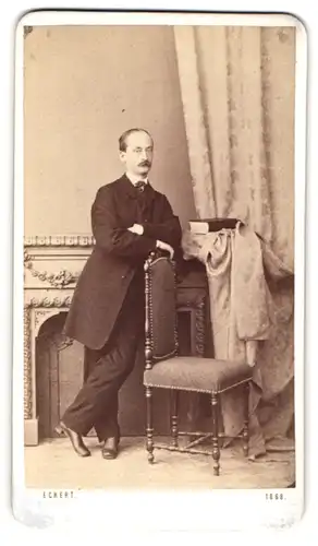 Fotografie H. Eckert, Prag, Portrait Herr im dunklen Anzug mit Moustache lehnt an einem Stuhl