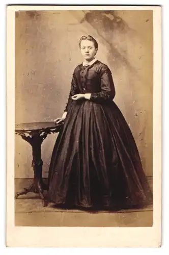 Fotografie H. Mencke, Itzehoe, junge Dame im schwarzen Kleid posiert an einem Tisch