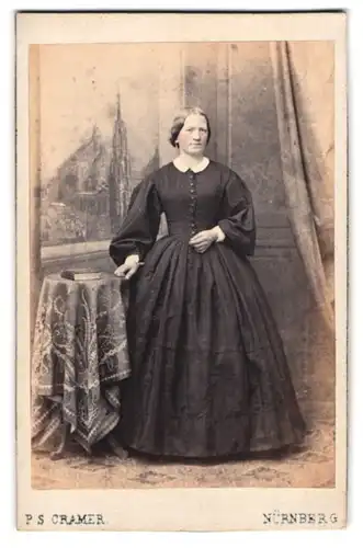 Fotografie P. S. Cramer, Nürnberg, junge Frau im dunklen Kleid mit Ohrringen vor einer Studiokulisse