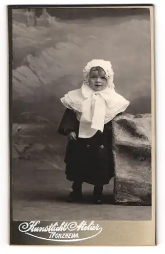 Fotografie Wronker, Pforzheim i. B., niedliches Kind im Winterkleid mit weisser Haube