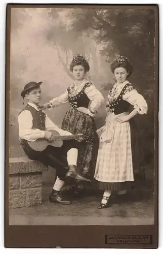 Fotografie Ludwig Giesecke, Erlangen, junger Mann mit zwei Damen in Trachtekleidern spielen Musik