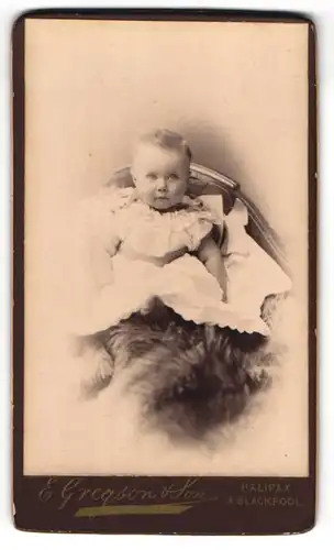 Fotografie E. Gregson & Son, Halifax, niedliches Kleinkind im weissen Kleidchen sitzt auf einem Fell