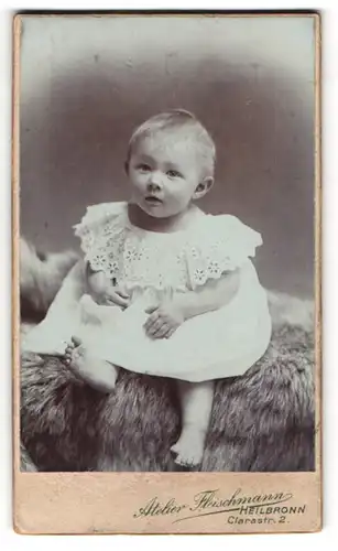 Fotografie Atelier Fleischmann, Heilbronn, niedliches Kleinkind im weissen Kleidchen auf Fell sitzend