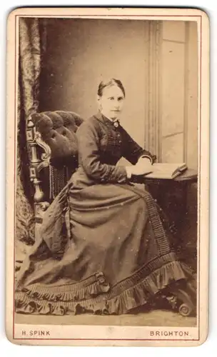Fotografie H. Spink, Brighton, Dame posiert sitzend im Kleid mit offenem Buch