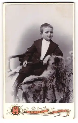 Fotografie Th. Alfred Hahn, Chemnitz, Portrait junger Knabe im Anzug liegt auf einem Fell
