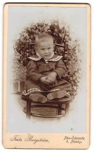 Fotografie Fritz Bergström, Neu-Ödernitz, Kleiner Junge im Kleidchen sitz auf einem Stuhl