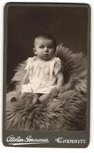 Fotografie Atelier Germania, Chemnitz, Kleinkind im weissen Kleidchen sitzt auf Fell
