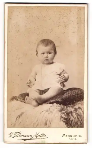 Fotografie G. Tillmann-Matter, Mannheim, Heidelbergerstrasse, Pummeliges Kleinkind in weisser Kleidung sitzt auf Kissen