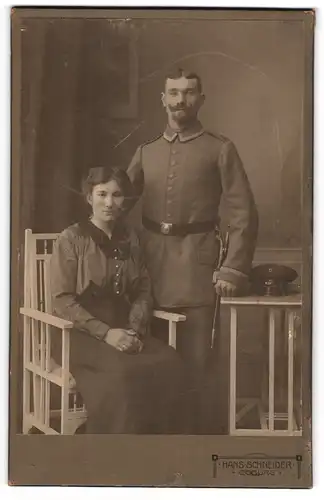 Fotografie Hans Schneider, Coburg, Unteroffizier in Feldgrau mit Bajonett u. Portepee und Gattin in der Küche