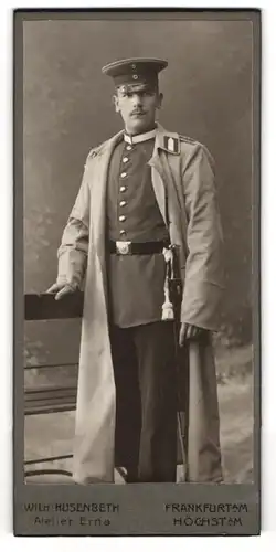 Fotografie Wilh. Husenberth, Frankfurt a. M., Kaiserstrasse 5a, Junger Soldat in Uniform mit Bajonett im Mantel