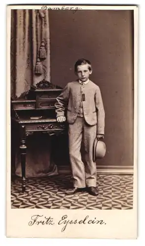 Fotografie R. Schade, Bayreuth, junger Knabe Fritz Eysselein im Anzug mit Hut am Sekretär