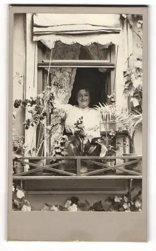 Fotografie unbekannter Fotograf und Ort, Frau schaut aus ihrem Fenster mit Vogelkäfig und Pflanzen bestückt