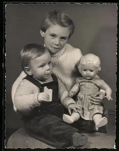 Fotografie Mädchen hat Puppe und Kleinkind auf dem Schoss sitzend