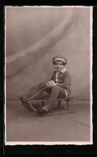 Foto-AK Mädchen sitzt auf Schlitten in einer Studiokulisse