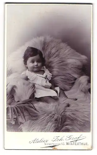 Fotografie Joh. Graf, Winterthur, Niedergasse 13, Niedliches Kleinkind im weissen Kleidchen auf Stuhl sitzend