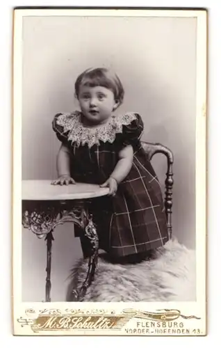 Fotografie M. B. Schultz, Flensburg, Norder-Hofenden 13, Niedliches junges Mädel im Kleidchen auf Stuhl stehend