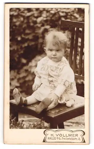 Fotografie H. Vollmer, Halle a. S., Freiimfeldstrasse 2, Kleinkind mit missmutigem Blick auf einem Stuhl im Garten
