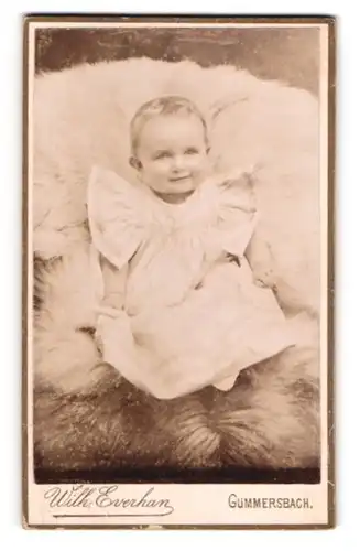 Fotografie Wilh. Everhan, Gummersbach, Süsses Kleinkind im Kleid sitzt auf einem Fell