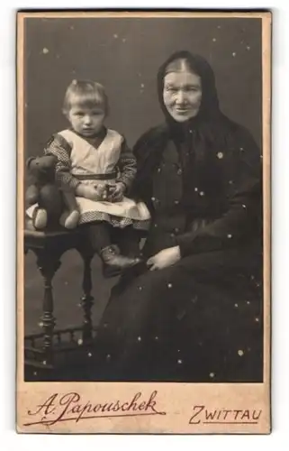 Fotografie A. Papouschek, Zwittau, Grossmutter mit Enkeltocher samt Teddybär auf dem Tisch