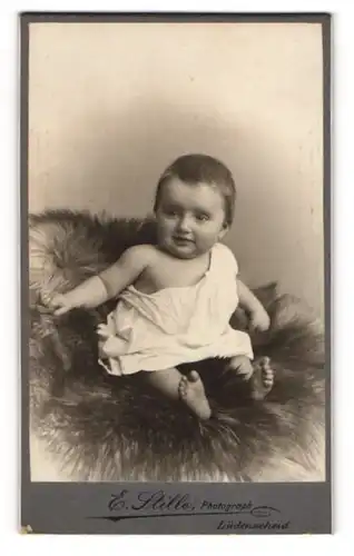 Fotografie E. Stille, Lüdenscheid, Süsses Kleinkind im weissen Kleidchen sitzt auf einem Stuhl