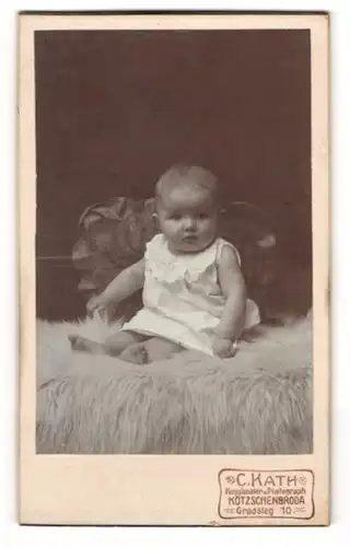 Fotografie C. Kath, Kötschenbroda, Gradsteg 10, Niedlicher Säugling im weissen Kleid sitzt auf einem flauschigen Teppich