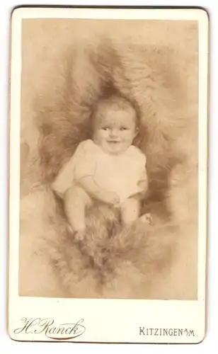Fotografie H. Ranck, Kitzingen a. M., Süsses Kleinkind im Hemd sitzt auf einem Fell