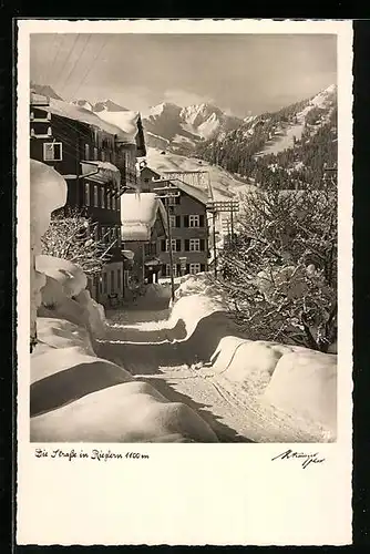 AK Riezlern, verschneite Strasse mit Häuserreihe in Berglandschaft