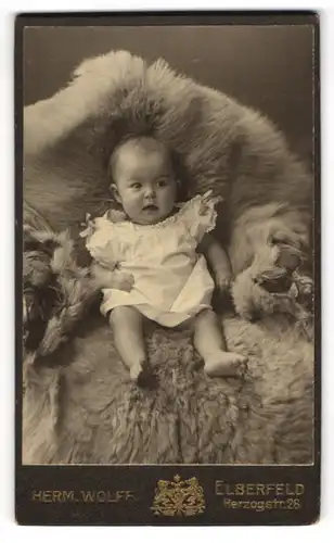 Fotografie Herm. Wolff, Elberfeld, Herzogstr. 28, Süsses Kleinkind im Hemd sitzt auf Fell