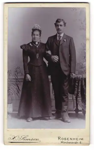 Fotografie X. Simson, Rosenheim, Münchenerstr. 6, Eheleute um dunklen Brautkleid mit Kopfschmuck und im Anzug
