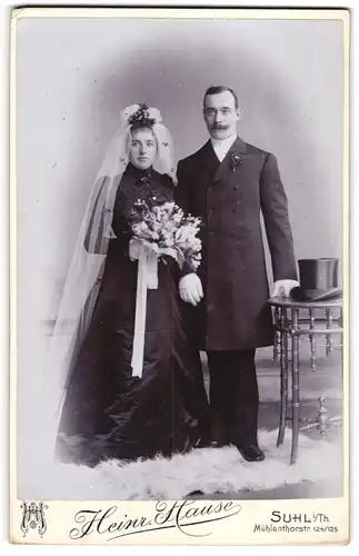 Fotografie Heinr. Hause, Suhl i. Th., junge Eheleute im schwarzen Brautkleid und Anzug mit Zylinder auf dem Tisch