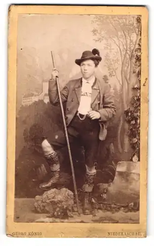 Fotografie Georg König, Niederaschau, junger Bayer in Tracht mit Lederhose und Wanderstock vor einer Studiokulisse