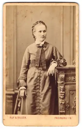 Fotografie Ruf & Dilger, Freiburg i. B., junge Dame im schlichten Kleid mit Schleife und geflochtenen Haaren