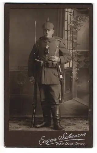 Fotografie Eugen Scheurer, Neu-Ulm, Soldat in Feldgrau Uniform mit Pickelhaube Tarn, Ausmarschgepäck, Kriegsausmarsch