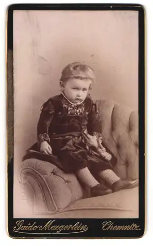 Fotografie Guido Maegerlein, Chemnitz, Niedliches Kleinkind im schwarzen Kleidchen sitzt auf Sessel