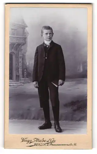 Fotografie Hugo Strube & Co., Berlin, Prinzessinnenstr. 16, Portrait frecher Bube im Anzug vor einer Studiokulisse