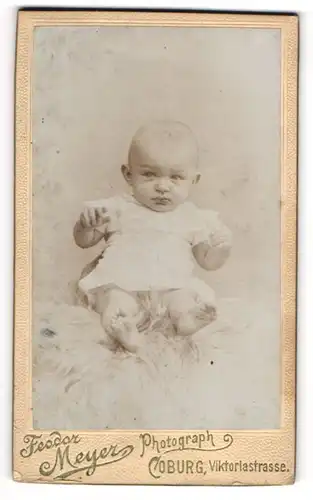 Fotografie Feodor Meyer, Coburg, Viktoriastr., Portrait süsses Baby im weissen Hemdchen auf Fell sitzend