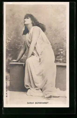 AK Schauspielerin Sarah Bernhardt, im weissen Kleid auf einer Mauer sitzend