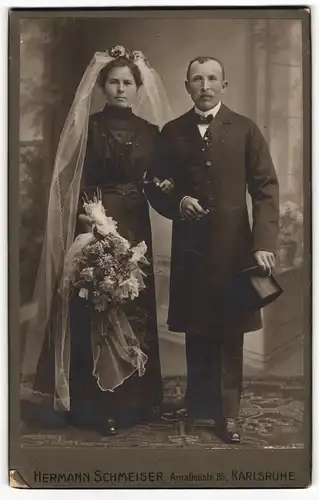 Fotografie Hermann Schmeiser, Karlsruhe, Ehepaar im schwarzen Brautkleid mit Schleier und Anzug mit Zylinder