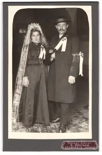 Fotografie G. Köstner, Kraiburg a. S., Hochzeitspaar im schwarzen Brautkleid und im Anzug mit Hut