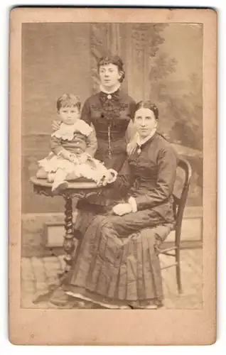 Fotografie unbekannter Fotograf und Ort, Zwei hübsche junge Damen mit einem kleinen Mädchen auf dem Tisch sitzend