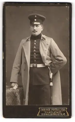 Fotografie Heinr. Fröhlich, Ingolstadt, Ziegelbräustrasse 4, Soldat in Mantel und Uniform mit Portepee am Bajonett